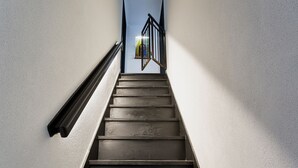 A staircase with a metal handrail and a view of a building through a window at the top.