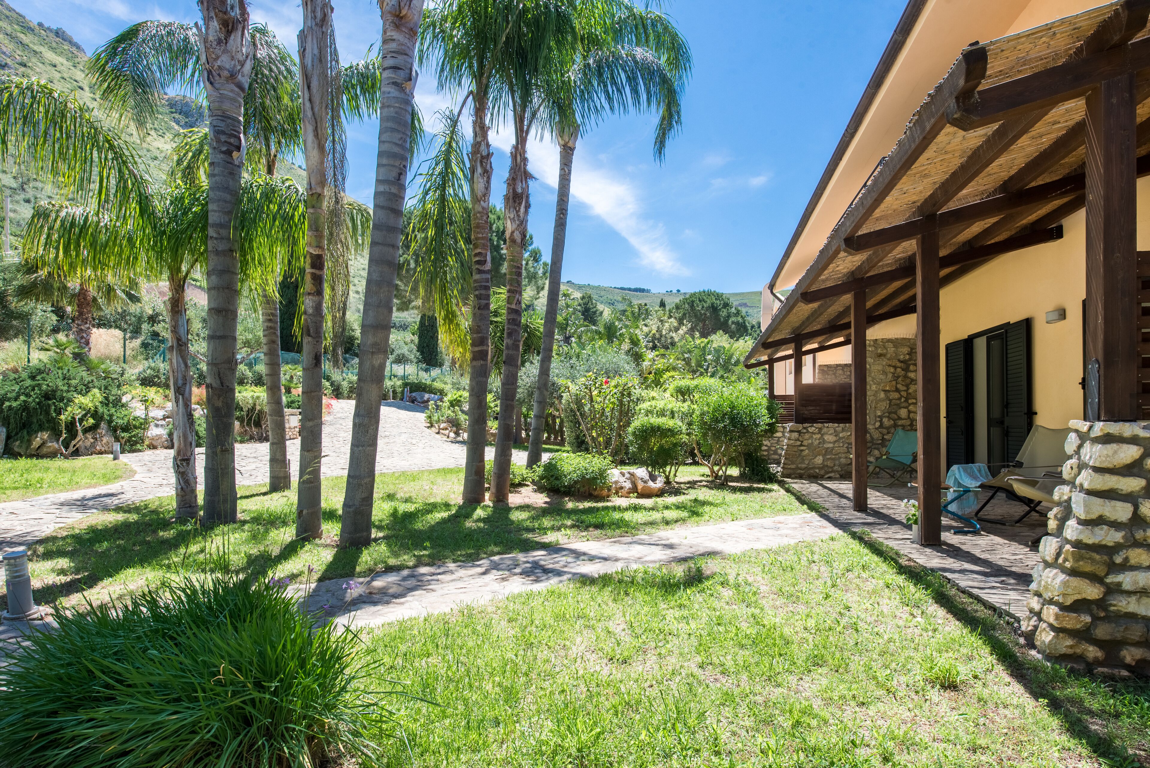 A courtyard with palm trees, a stone pathway, and a building with a covered patio area.