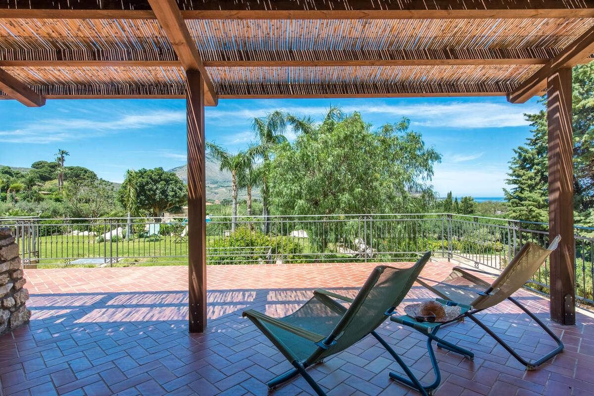 A covered outdoor area with two lounge chairs and a view of a landscaped garden and hills.