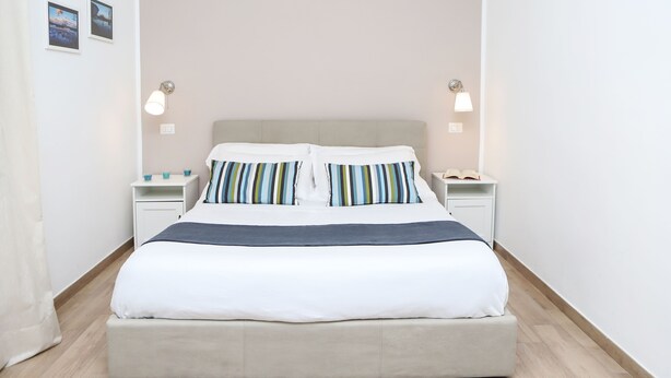 A neatly made bed with striped pillows, a bedside table with a lamp, and a nightstand with a phone.