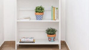 A white bookshelf with three shelves, each holding books and potted plants.