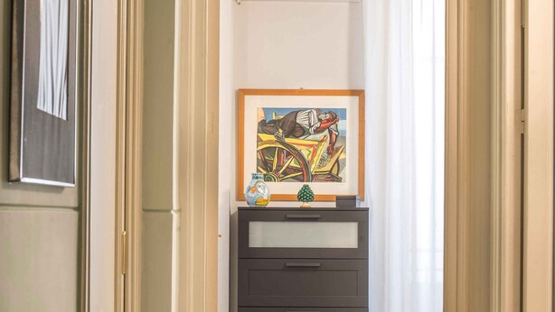 Een gang met een houten tafel, een lijstwerk met kunst, een donkere kast en een rood tapijt.