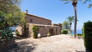 A stone building with a tiled roof, a paved courtyard, and a view of the sea. - Relax at the Swimming Pool by Wonderful Italy (Cefalù)