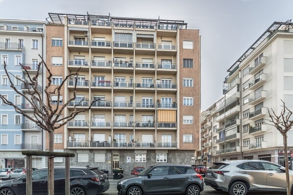 Un edificio residencial de varios pisos con balcones, coches aparcados y cielo despejado.