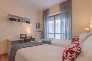 Una habitación de hotel con dos camas, un escritorio con ordenador, una silla y una ventana con cortinas.