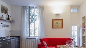 A compact living space with a kitchenette, a red sofa, a dining table with dishes, and a bookshelf. - Cozy Family Apartment in Castelletto by Wonderful Italy (Genoa)