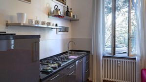 A kitchen with a stove, sink, and cabinets, a window with curtains, and artwork on the walls. - Cozy Family Apartment in Castelletto by Wonderful Italy (Genoa)