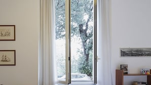 A bedroom with a large window, a radiator, a desk with a chair, a bookshelf, and a bed. - Cozy Family Apartment in Castelletto by Wonderful Italy (Genoa)