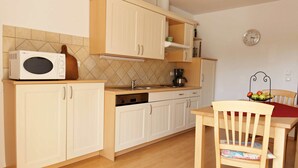 A compact kitchen with white cabinets, a microwave, a sink, and a dining area with a chair and table. - Ferienwohnung (Marquartstein)