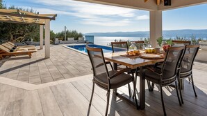 A covered outdoor dining area with a pool, wooden furniture, and a view of the sea. - Villa Dream with private pool, 2 bedrooms with en-suite bathrooms, sea view (Omis)
