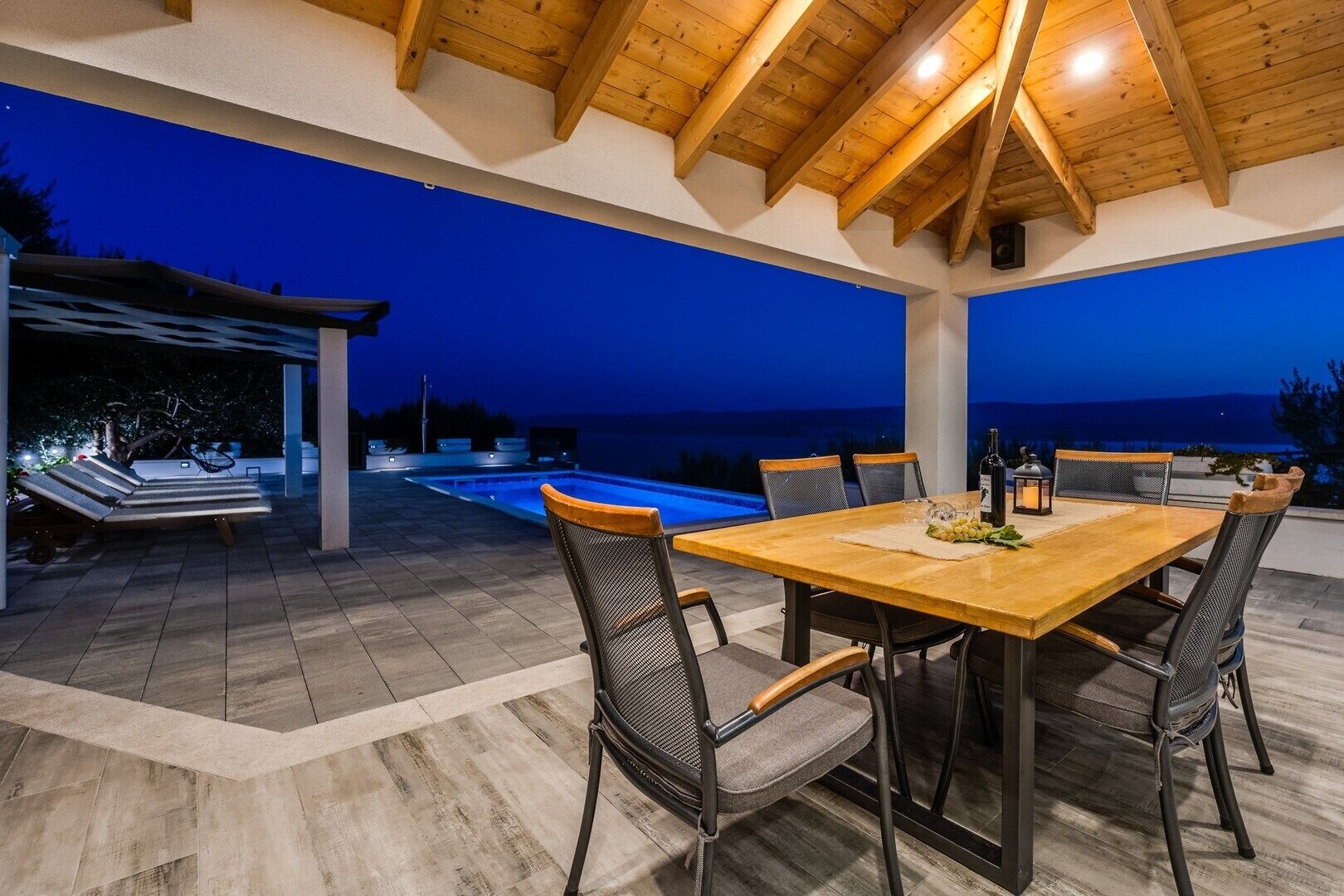 An outdoor patio with a pool, dining table, and chairs, overlooking a scenic view.