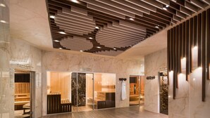 Un moderno espacio de spa con bancos de madera, entrada por puerta de vidrio y suelo de mármol.