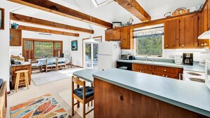 Une cuisine spacieuse avec des poutres en bois, un grand îlot central et une vue sur l’extérieur.