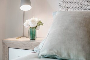 A bedside table with a vase of white flowers, a lamp, and a pillow. - Syros Apartment (Javea / Xàbia)