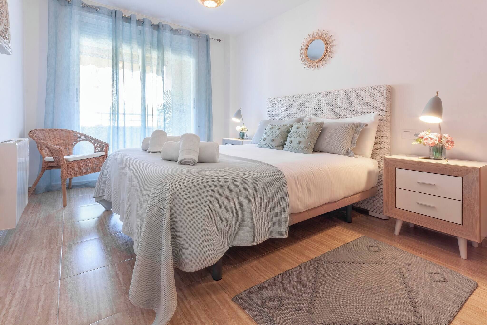 A neatly arranged bedroom with a bed, bedside tables, a chair, and a large window with curtains.