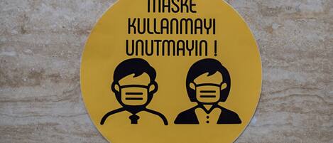A yellow circular sign with two figures wearing masks and the text "MASKE KULLANAYI UNUTMAYIN!"