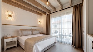 Un dormitorio con una cama grande, vigas de madera en el techo, dos apliques de pared, una mesita de noche y vistas a un balcón exterior.