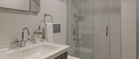 A modern bathroom with a white sink, mirror, and toilet, a glass shower enclosure, and patterned floor tiles.