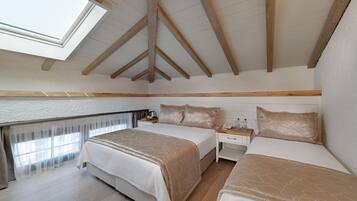 A bedroom with two beds, a skylight, wooden beams, a bedside table with a lamp, and a window with sheer curtains.
