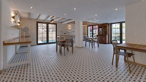 Una cocina amplia con electrodomésticos modernos, un comedor con mesas y sillas de madera, y ventanas grandes que ofrecen luz natural.