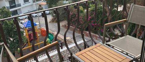Un balcón con vista al mar, una zona de juegos y un edificio con balcones.