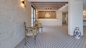 Un vestíbulo de hotel con una pared de ladrillo, piso estampado y una mesa de recepción con un cartel.