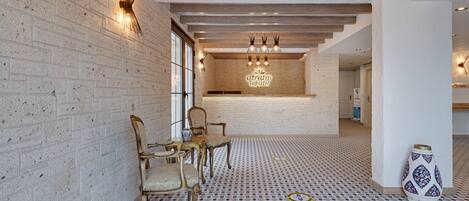 A hotel lobby with a brick wall, patterned floor, and a reception desk with a sign.