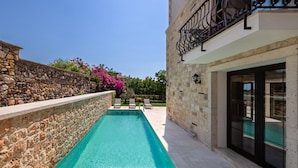 Piscina con paredes de piedra, mobiliario de exterior y balcón con barandillas de hierro forjado.