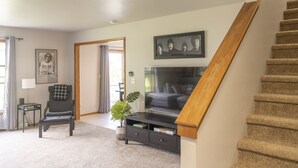 Un salon comprenant un canapé, un téléviseur, un escalier et une porte donnant sur une autre pièce.