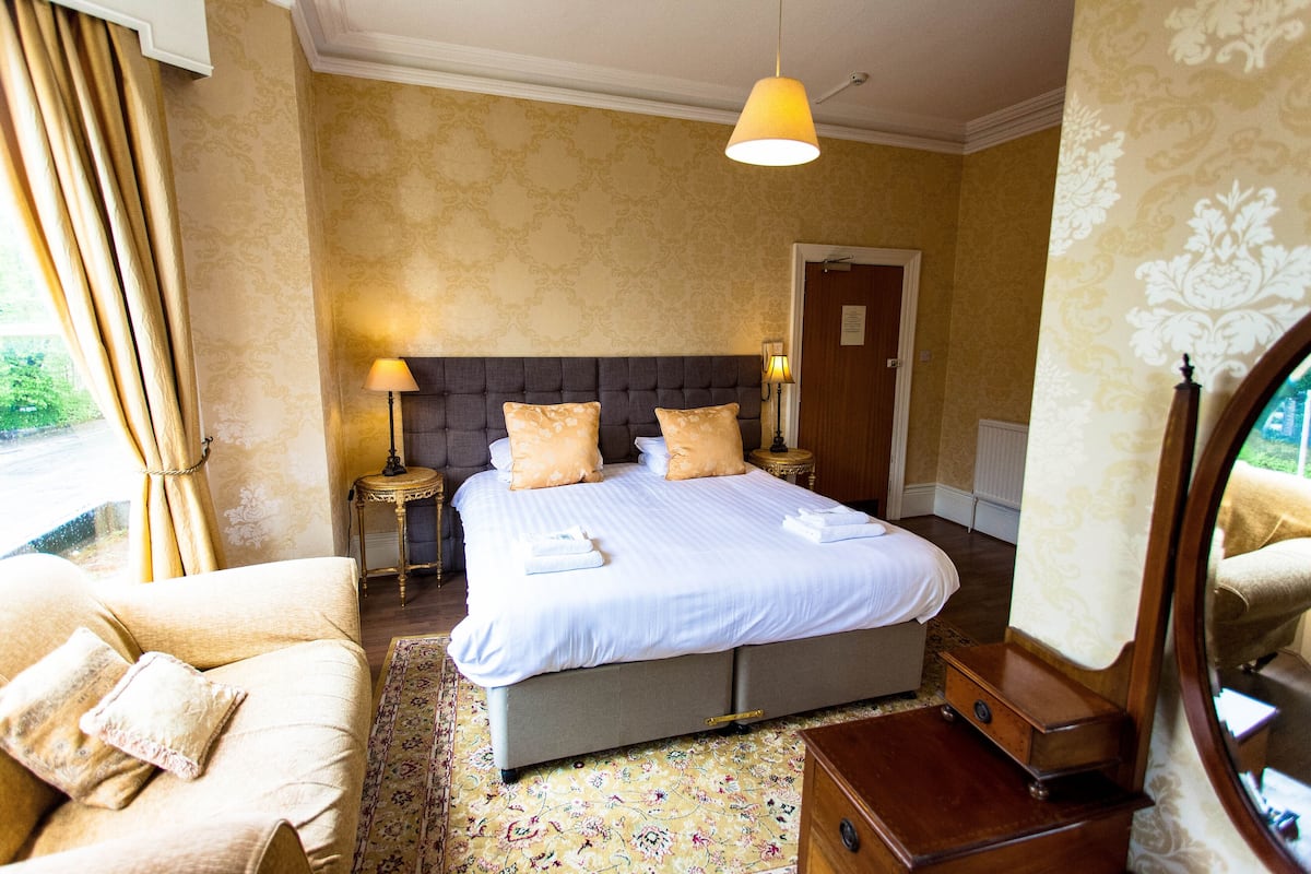 A hotel room with a large bed, two bedside tables, a nightstand, a dresser, and a mirror.