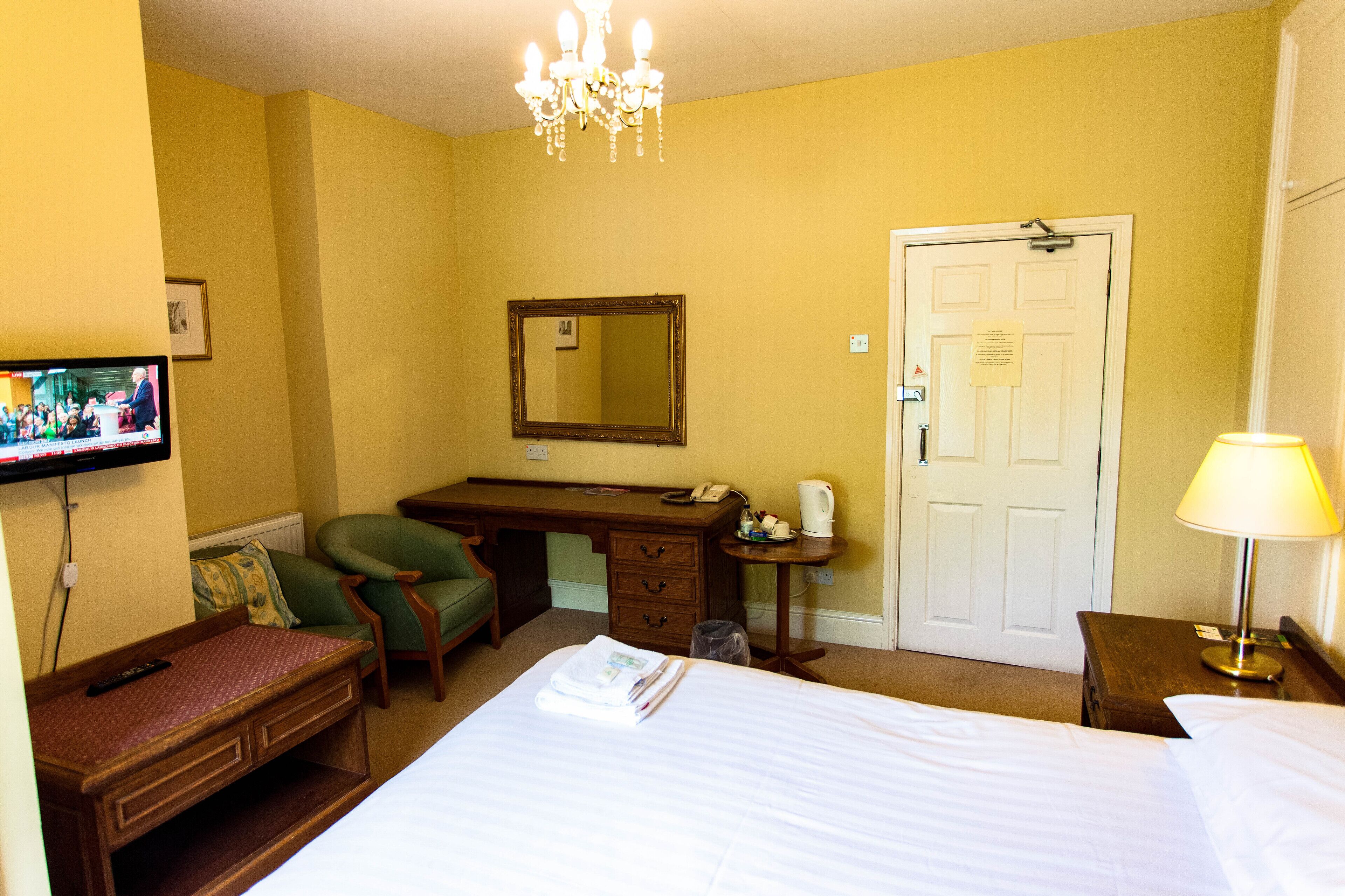 A hotel room with a bed, a desk, a chair, a television, and a door.