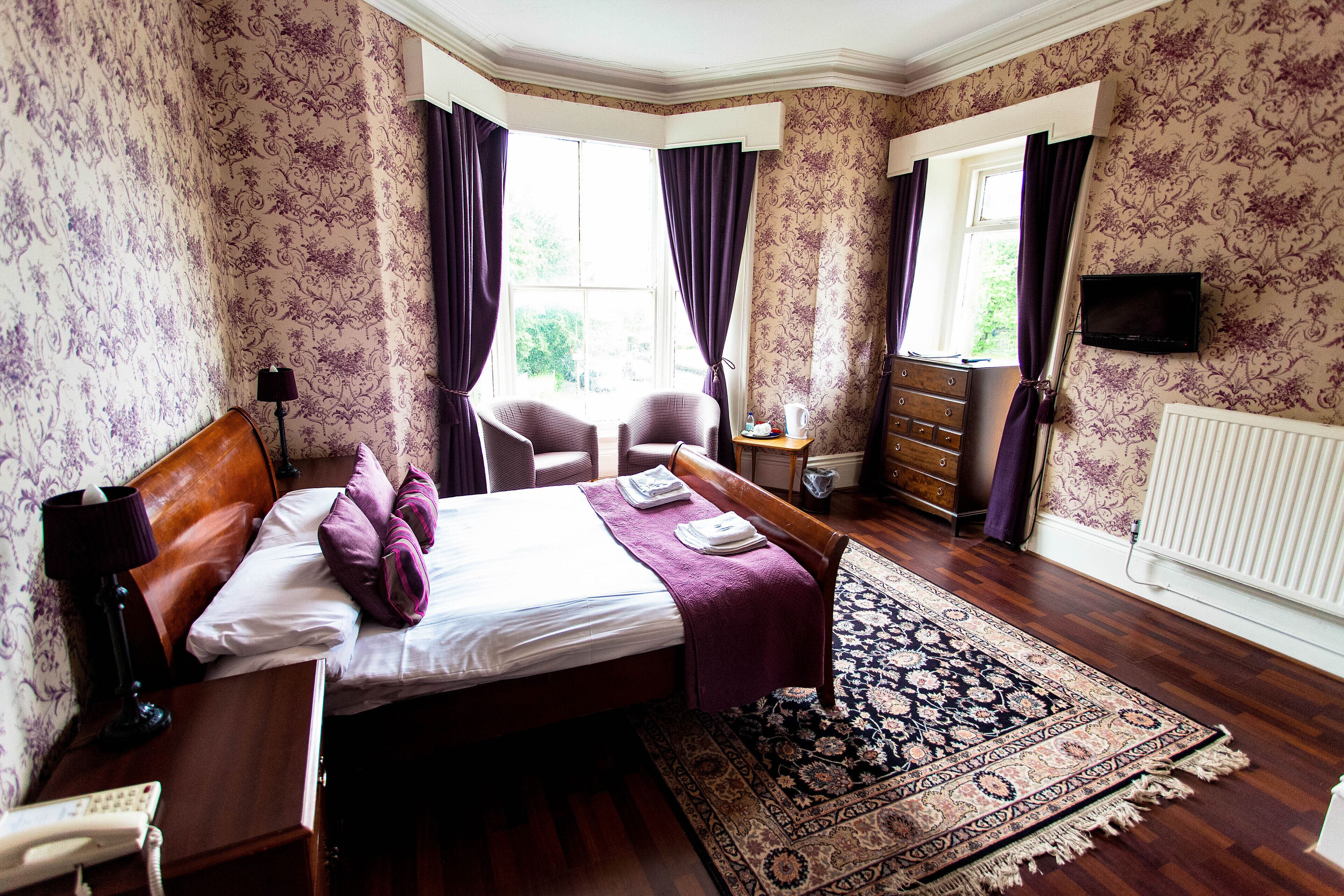 A hotel room with a bed, a chair, a dresser, a television, and a window with curtains.