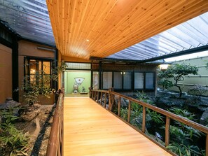 Un sentiero in legno conduce a una tradizionale sala giapponese con pavimento in tatami, paravento shoji e giardino roccioso.