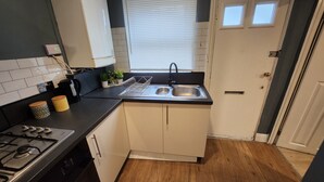A compact kitchen with a gas stove, a sink, and a window with blinds. - Apartment in london 2 minute walk to metro, near Stratford 

 (London)