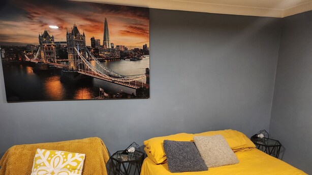 A bedroom with two beds, each with a different colored blanket and pillow. There is a large cityscape painting on the wall. - Apartment in london 2 minute walk to metro, near Stratford 

 (London)