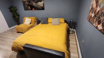 A bedroom with a large bed, two bedside tables, a nightstand, a wall-mounted picture, and a potted plant.