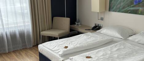 A hotel room with two beds, a desk, a chair, a lamp, and a painting on the wall.