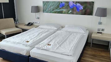 Ein Doppelbett mit weißer Bettwäsche, zwei Nachttische mit Lampen, ein an der Wand befestigtes Telefon und ein großes, gerahmtes Bild mit Blumen.