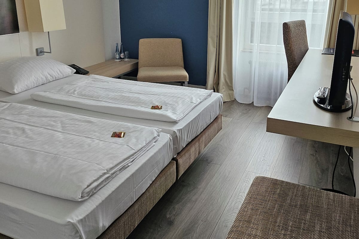 A hotel room with two beds, a desk, a chair, and a TV.