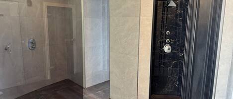 Un baño moderno con ducha envuelta en vidrio, tocador de mármol y pared de acento en mármol negro.