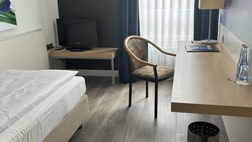 Una habitación de hotel con cama, escritorio, silla, televisor y lámpara.