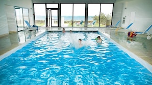 An indoor swimming pool with clear blue water, large windows, and lounge chairs. - Apartment in Plougasnou With Stunning Sea Views (Plougasnou)