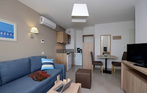 A modern living room with a sofa, a coffee table, a TV, and a dining area with a table and chairs. - Beautiful Apartment Near Port-barcares Beach (Le Barcares)
