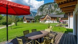 A wooden deck with outdoor furniture, a red umbrella, and a view of mountain houses. - Chalet in Obertraun Near Krippenstein Ski Area (Obertraun)