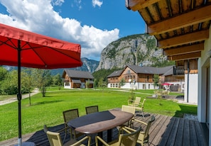 A wooden deck with outdoor furniture, a red umbrella, and a view of mountain houses. - Chalet in Obertraun Near Krippenstein Ski Area (Obertraun)