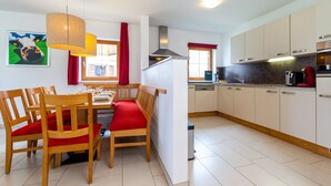 A dining area with wooden chairs and a bench, a kitchen with white cabinets, and a painting on the wall. - Chalet in Obertraun Near Krippenstein Ski Area (Obertraun)