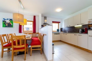 A dining area with wooden chairs and a bench, a kitchen with white cabinets, and a painting on the wall. - Chalet in Obertraun Near Krippenstein Ski Area (Obertraun)