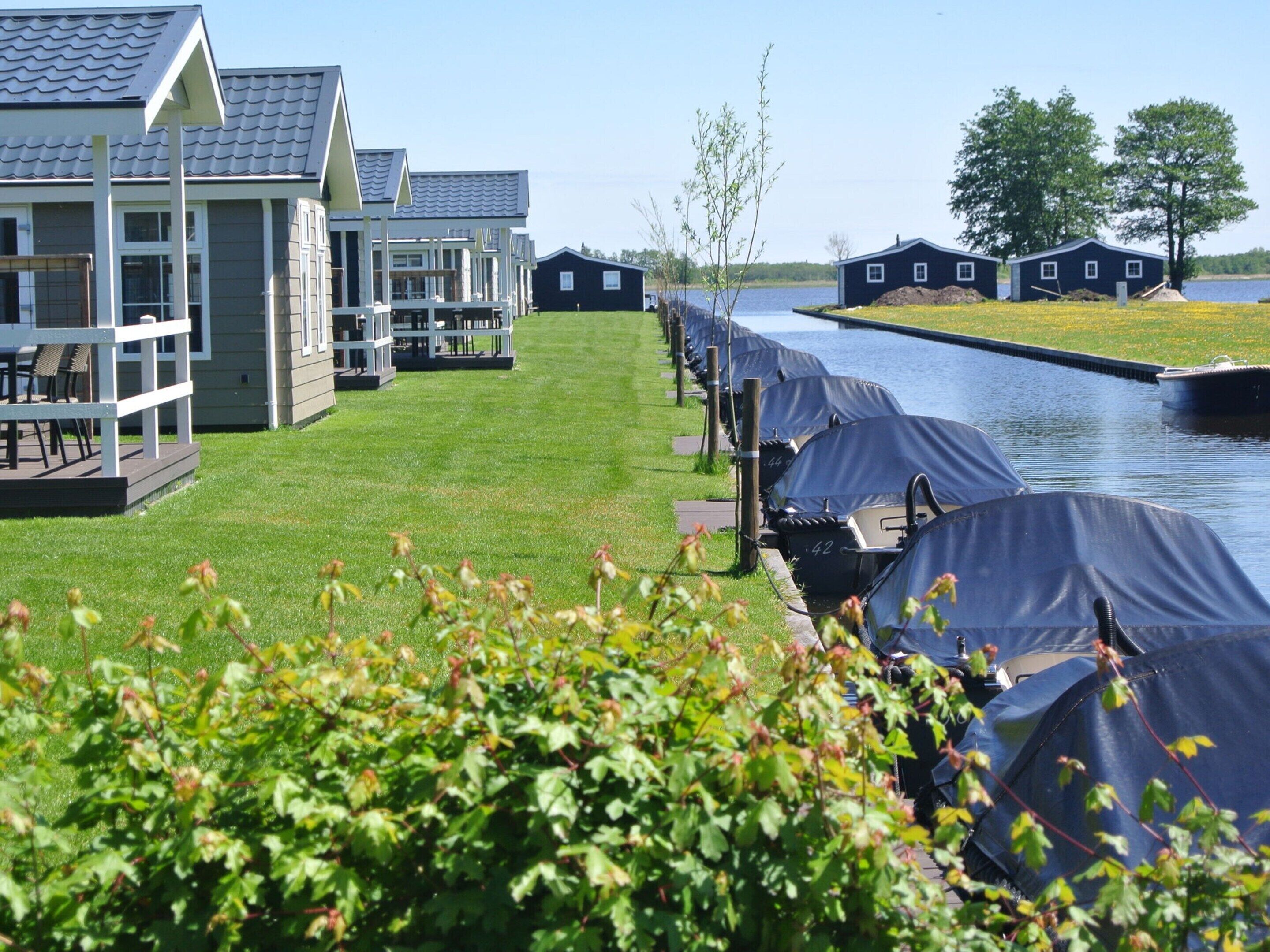 A row of cabins with a canal view, a grassy lawn, and a small dock area.