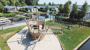 A playground with a wooden ship structure, a sandy play area, and a water body. - Lakeside Cottage With Boat (Giethoorn)
