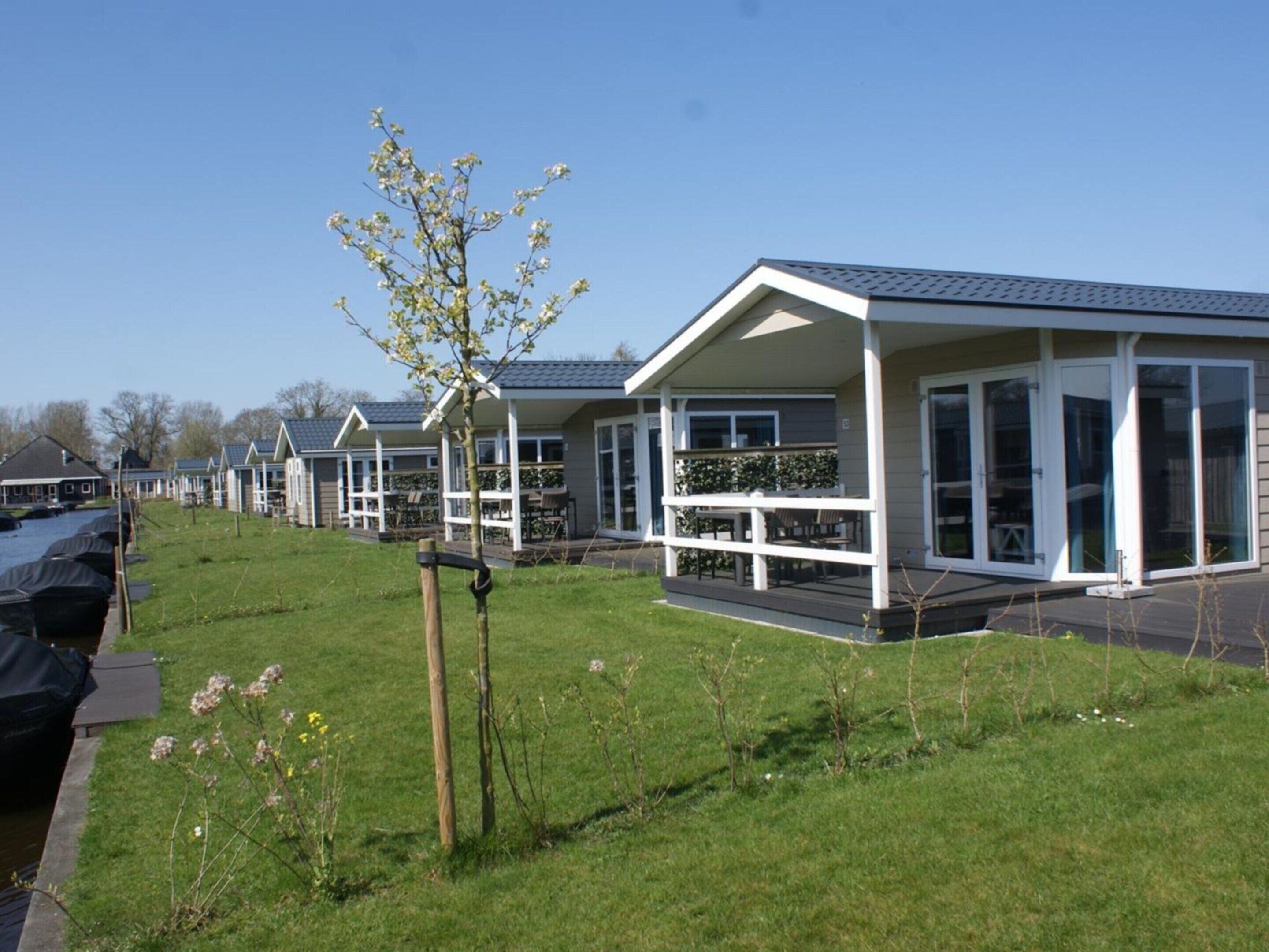 Een rij moderne vakantiehuisjes met grote ramen en balkons, gelegen naast een waterpartij.